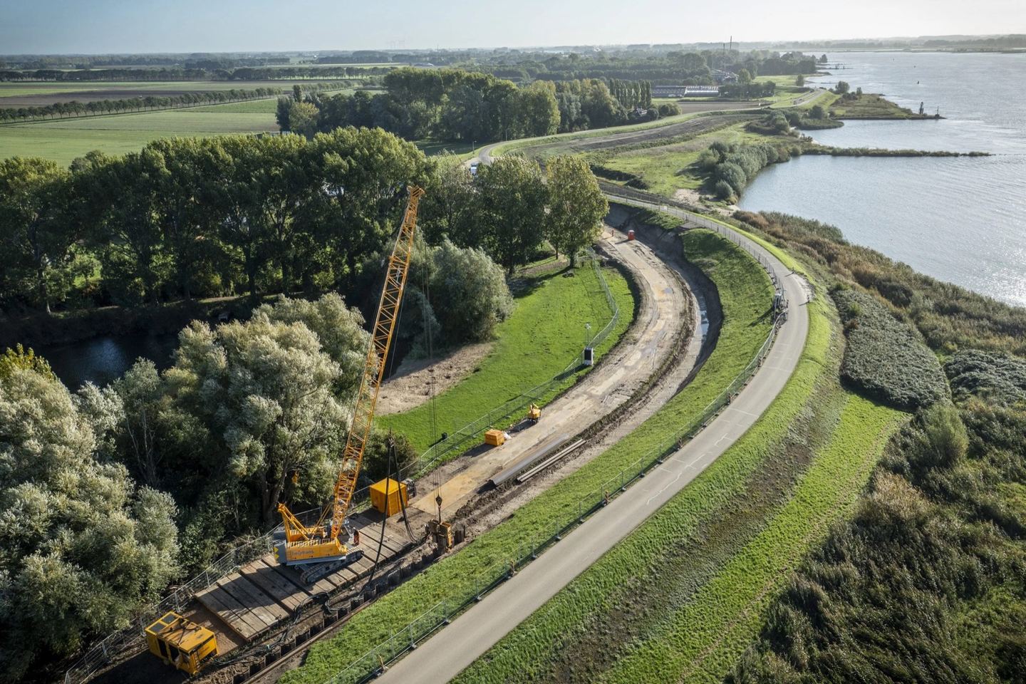 Luchtopname van een dijkversterkingsproject met bouwweg en kraan