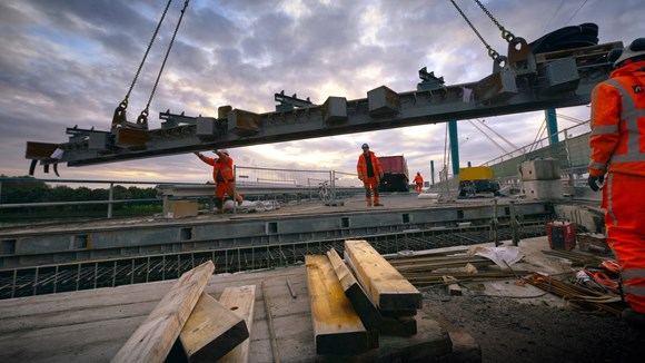 Brugbouw: een ligger wordt ingehesen terwijl bouwvakkers toekijken